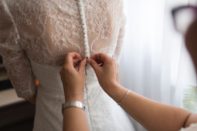 Ruce zapínající knoflíky na šatech nevěsty